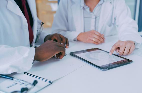 Close up of two physicians reviewing patient medical information or medical research on a pad.