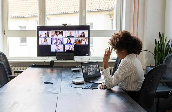 Woman meeting with colleagues over a video conference call using a laptop and big screen monitor