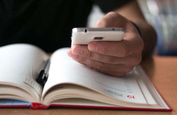 A man looks at his smartphone while making notes in his paper calendar.