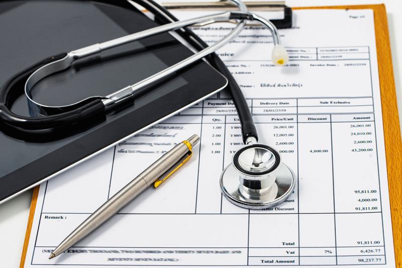 Stethoscope, pen and tablet placed on printout of a bill