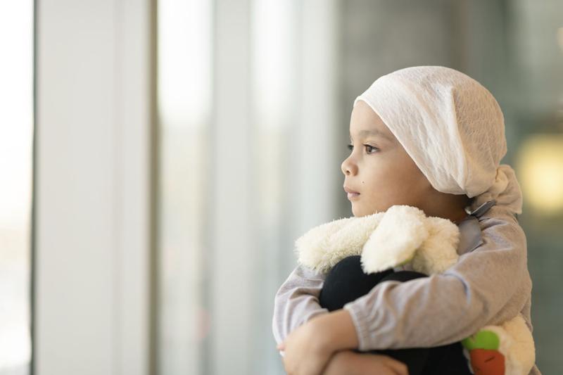Young patient wearing a headscarf and hugging a stuffed rabbit toy