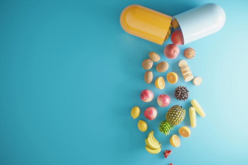 An open vitamin capsule spills out foods, fruits