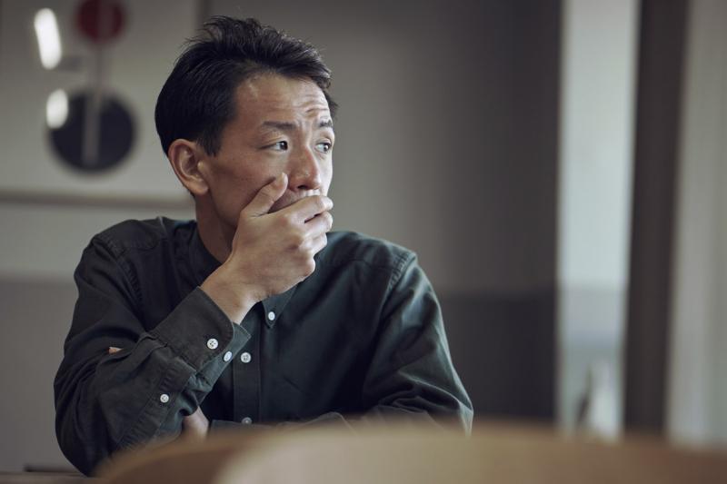 Man sits at table, hand covering mouth